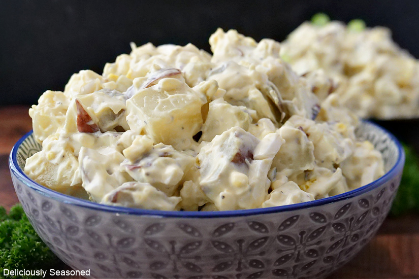A horizontal picture of red skinned potato salad in a patterned bowl with blue trim.
