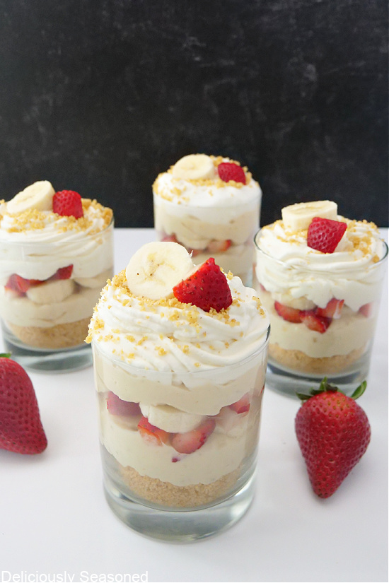 Four parfaits on a white table, with strawberries around them for decoration.
