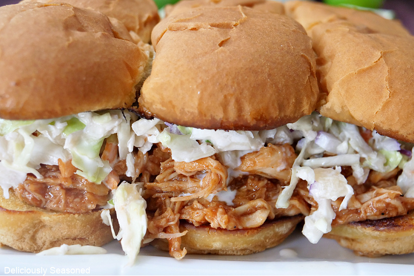 Three sliders on a white plate showing the shredded chicken filling and pineapple slaw.