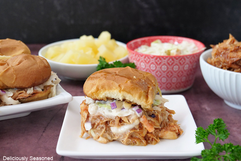 Two white plates with shredded chicken sliders on them.