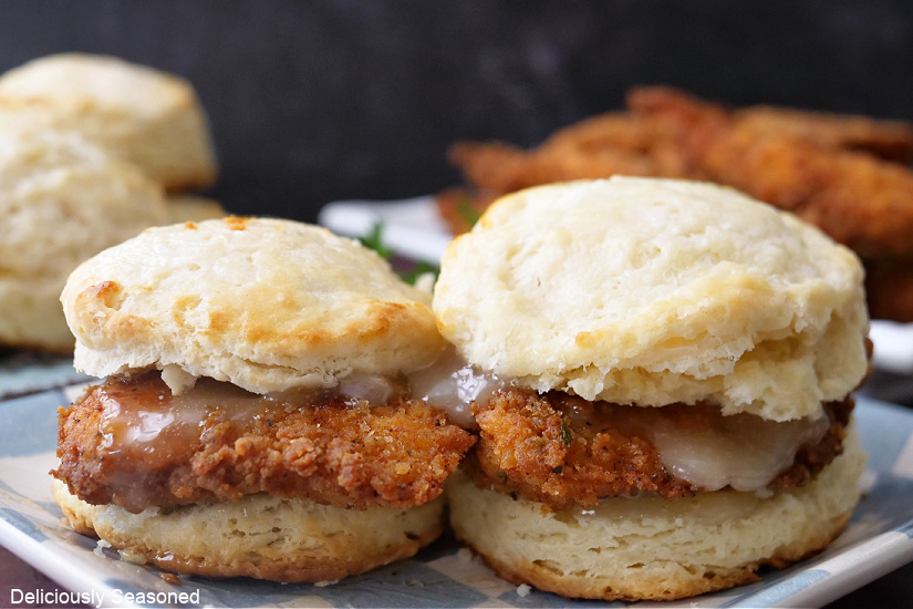 A landscape photo of two biscuits on a plate, with crispy chicken and honey butter on top.