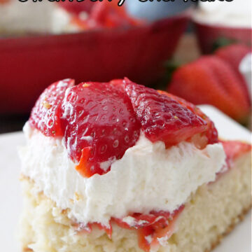 A slice of strawberry shortcake on a white plate, topped with whipped cream and fresh strawberries.