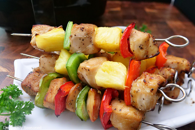 A landscape photo of kabobs stacked up on a square white plate.