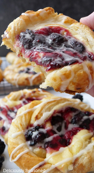 A close up of a blackberry pastry with a bite taken out of it held up to the camera.