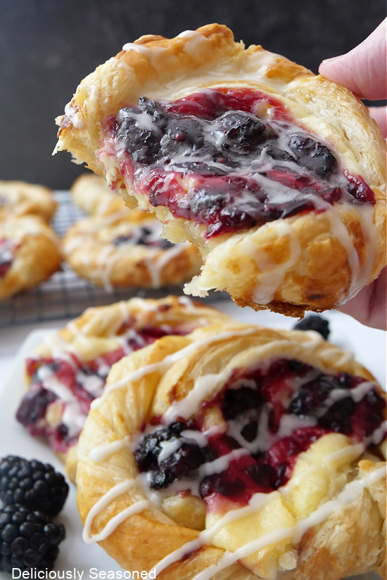 A close up of a pastry filled with blackberries and cream cheese with a bite taken out of it with more pastries on a plate below.