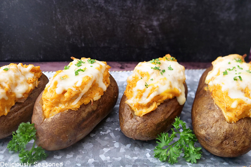 Baked potatoes lined up on a plate, topped with melted cheese.