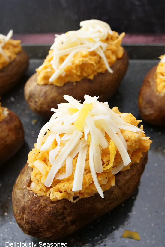 A close up photo of baked potatoes on a baking sheet with freshly shredded cheese on top.