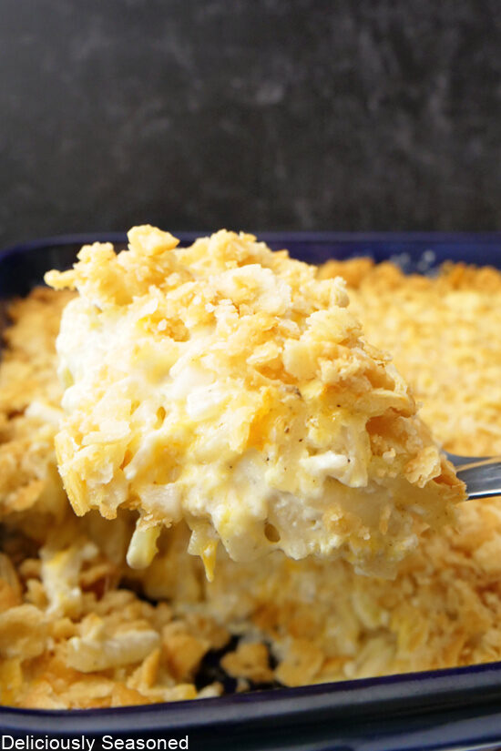 A large spoonful of funeral potatoes being scooped out of the baking dish.