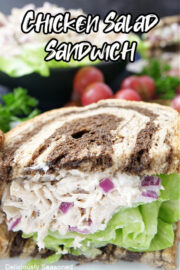 Half of a chicken salad sandwich facing forward on a plate, showing the chicken salad inside the pumpernickel bread.