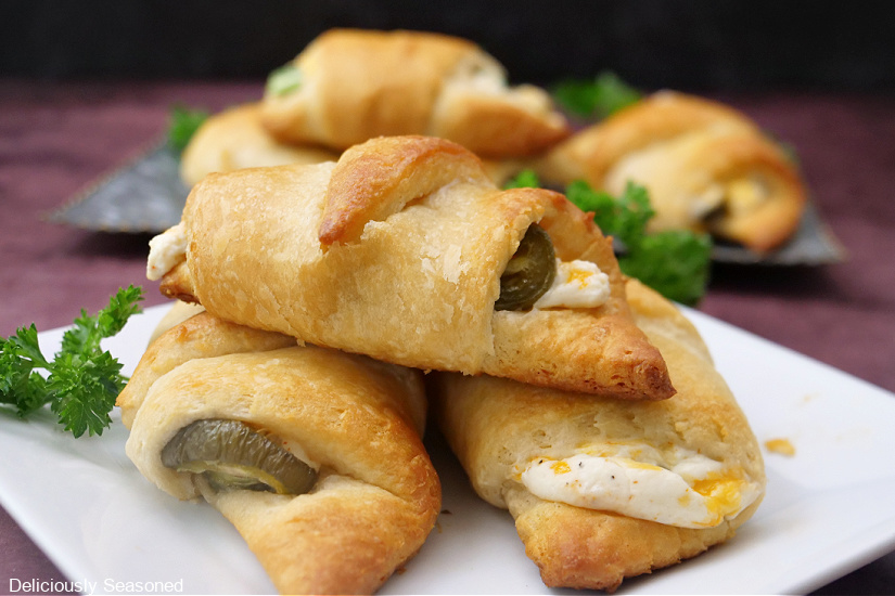 A landscape photo of a square plate with crescent rolls on with cream cheese and jalapenos in the middle.