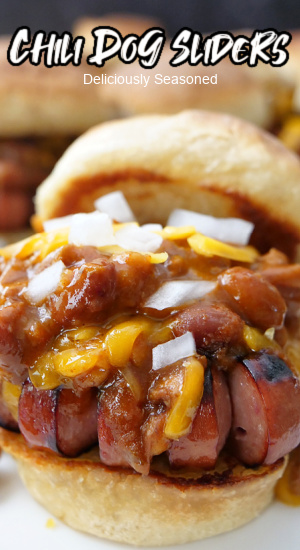 A close up of a slider with chili, cheese, onions and hot dog.