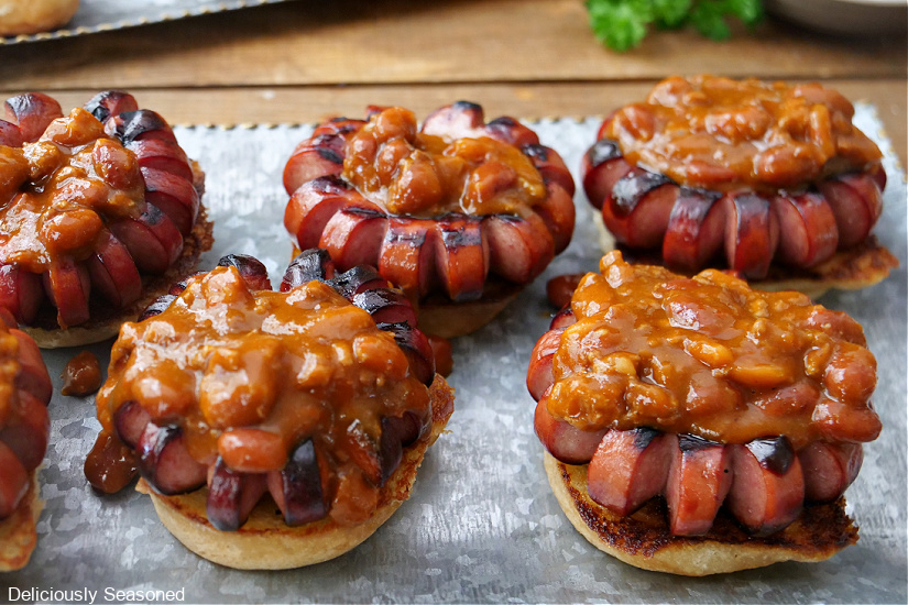A sliver platter with circular grilled hot dogs on top of a slider bun with chili on top.