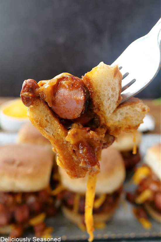 A bite of a chili dog slider on a fork being held close to the camera for a close up shot.