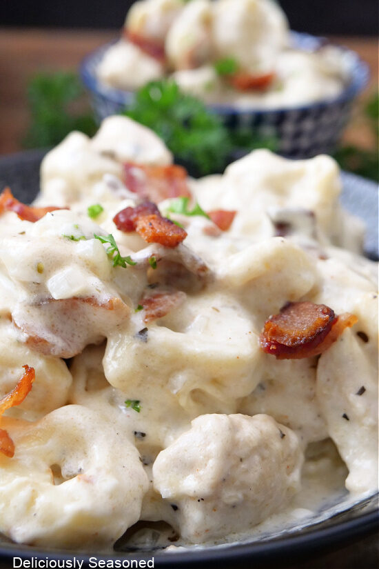 A close up of tortellini, bite-size chicken and crispy bacon in a creamy sauce in a black bowl.