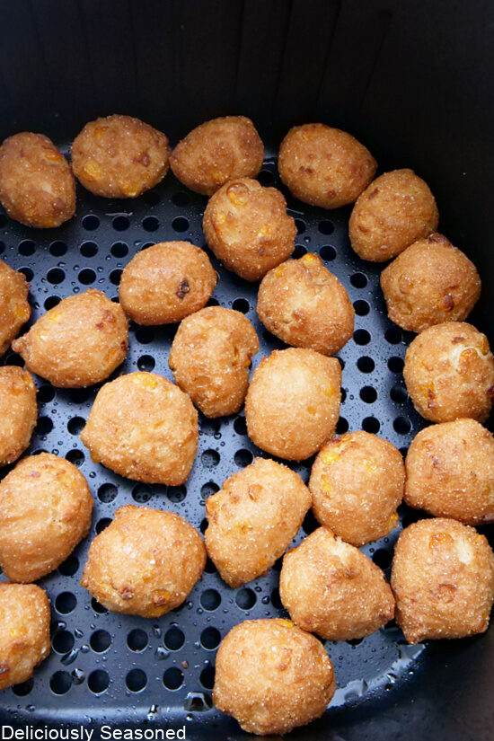 An air fryer basket with corn hushpuppies in it after cooking.