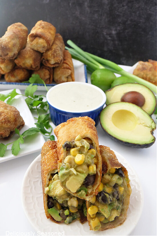 Avocado egg rolls on a small white plate with more egg rolls in the background.