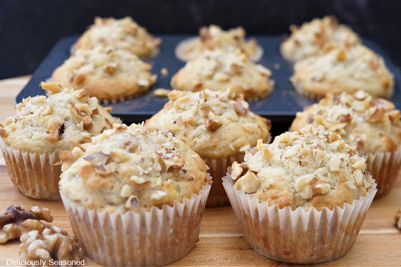 11 banana nut muffins on a wood surface and some in a muffin tin.