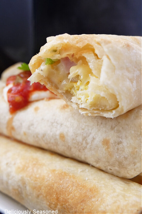 A close up of flautas stacked on each other and the top flauta has a bite taken out of it.
