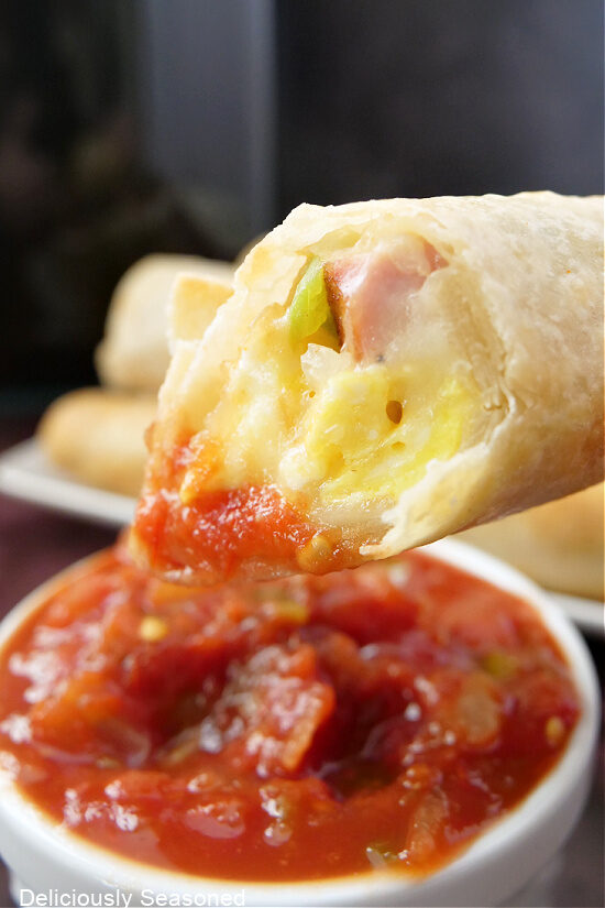 A close up photo of a flour tortilla filled with scrambled eggs, ham and cheese, that has been dipped in salsa.