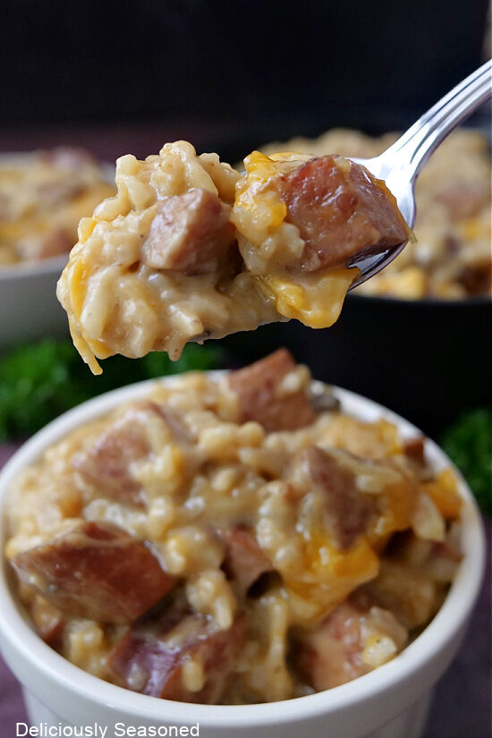 A close up of a spoonful of sausage and rice casserole held above a white bowl with a serving in it. 