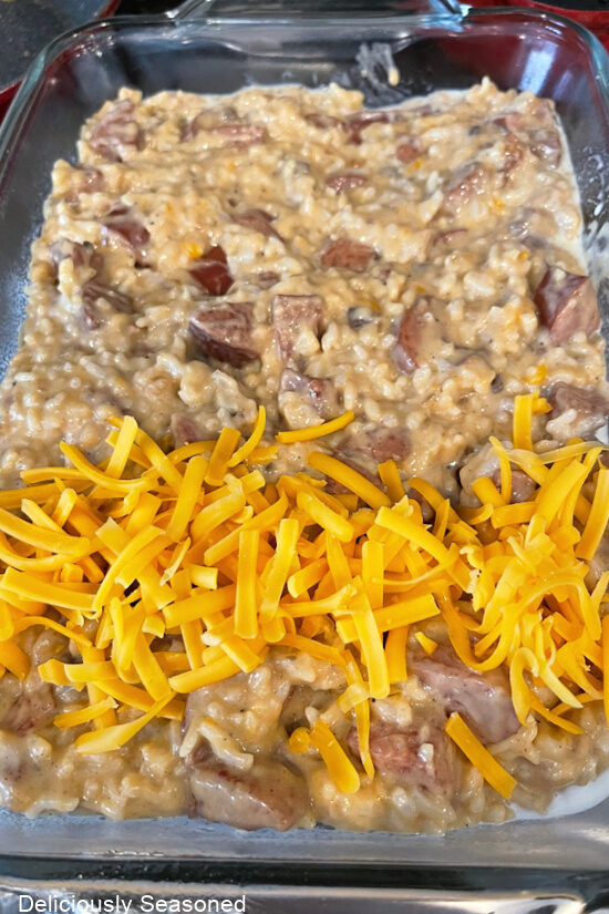 A glass baking dish with the casserole in it, being topped with cheese and about to go in the oven.