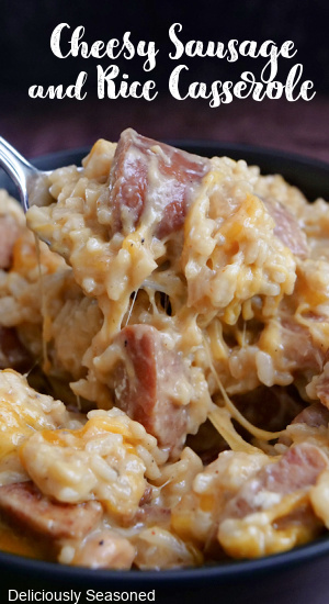 A spoonful of cheesy sausage and rice being scooped from the bowl.
