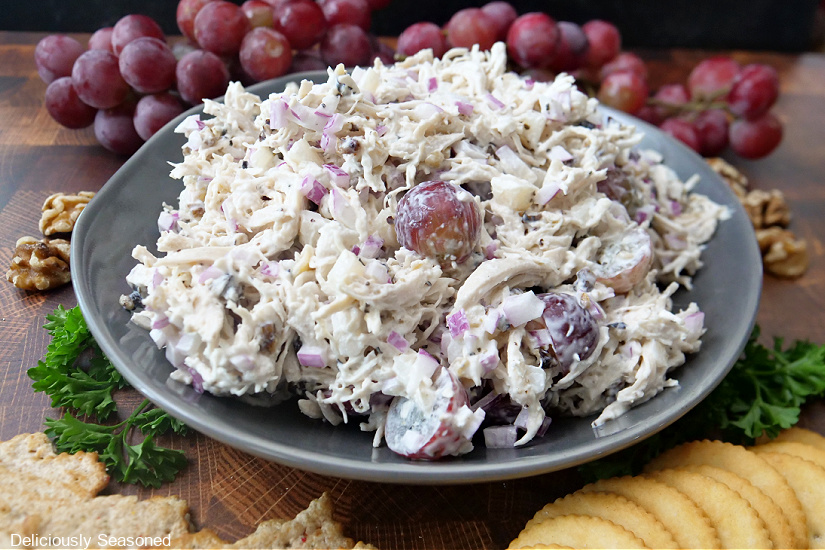 A landscape photo of a large bowl of chicken salad with walnuts and grapes in the background.