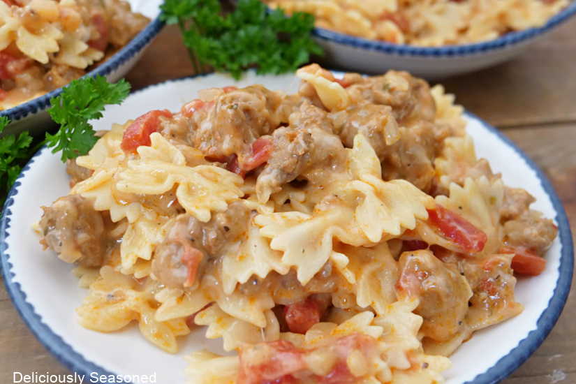A serving of Italian sausage bow tie pasta in a white bowl with blue trim.