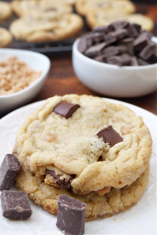 Two cookies on a white plate with pieces of chocolate chunks on the plate too.