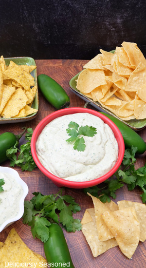 An overshot of creamy jalapeno dip with tortilla chips and jalapenos and cilantro placed around the dip bowl.