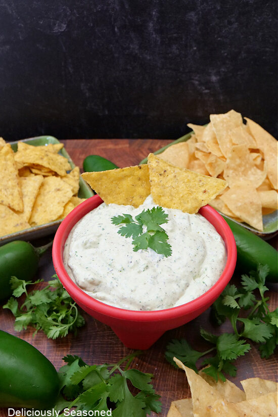 A red bowl with jalapeno cilantro dip in it with tortilla chips on two plates.