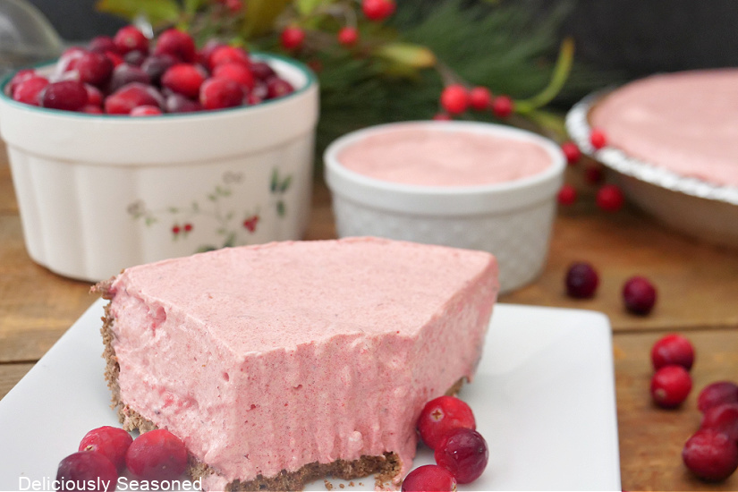A horizontal photo of a slice of no bake cranberry raspberry pie on a white square plate.