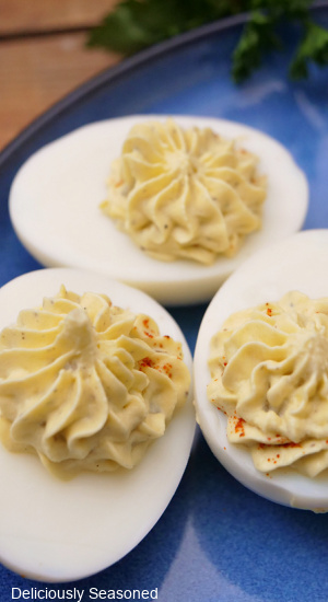 A close up of three deviled eggs on a blue plate.