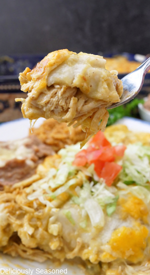 A bite of enchiladas on a fork held above a plate with more enchiladas.