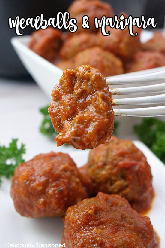 A homemade meatball on a fork with a bite taken out of it with more meatballs on a white plate.
