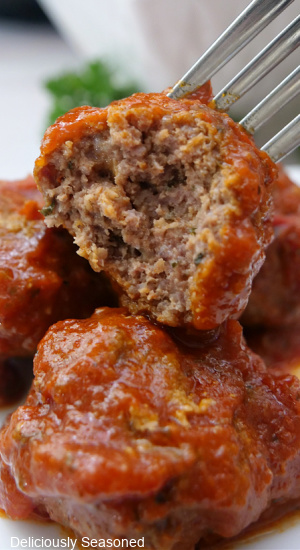 A close up of a meatball on a fork with a bite taken out of it.