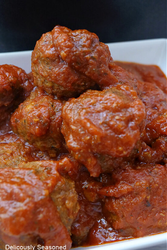 A close up of a white bowl of meatballs and marinara sauce.