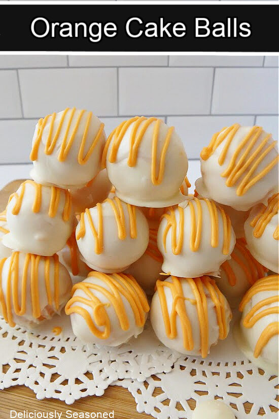 A stack of orange cake balls on a wood surface with white paper doilies underneath. 