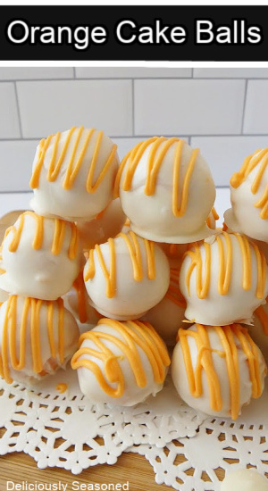 A stack of orange flavored cake balls on white paper doilies and on top of a wood surface.