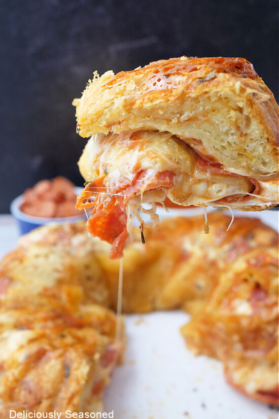 A close up of a piece of crescent roll pepperoni pizza being held up showing the cheese, pepperonis and the crescent roll.