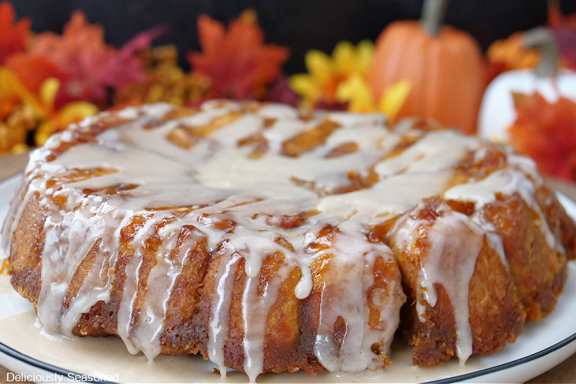 A white plate with pumpkin spice monkey bread on it with fall foliage in the background.