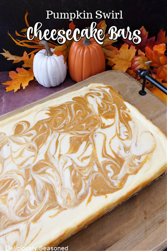 A wood cutting board with a whole uncut pumpkin swirl cheesecake on it.