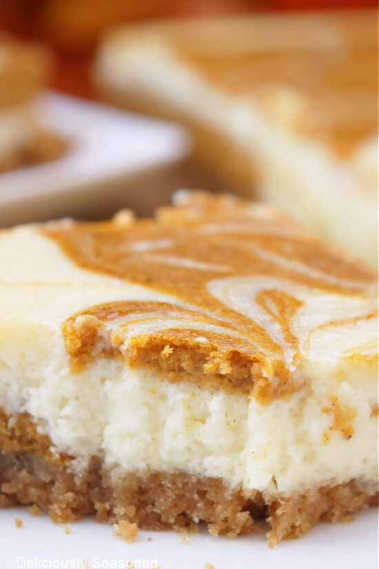 A close up of a serving of pumpkin cheesecake bar with a bite taken out of it.