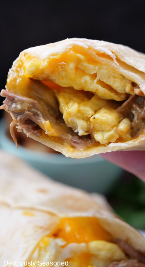 A breakfast burrito held close to the camera showing the ingredients in the burrito.