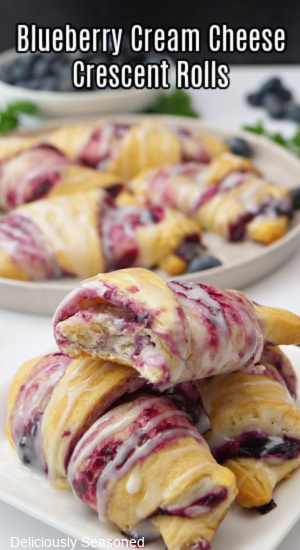 Blueberry crescent rolls stacked on a plate with a bite taken out of the top one.