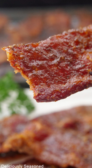 A piece of candied bacon being held close to the camera lens.