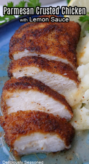 A piece of parmesan crusted chicken, sliced on a blue plate and served next to mashed potatoes.