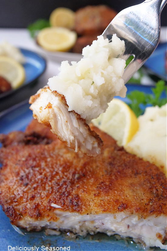A bite of lemon chicken on a fork with mashed potatoes.