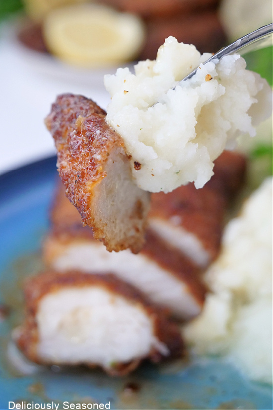 A bite of chicken on a fork with mashed potatoes. 