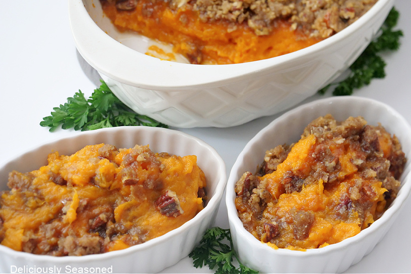 A horizontal photo of three white oval bowls with sweet potato casserole in them.